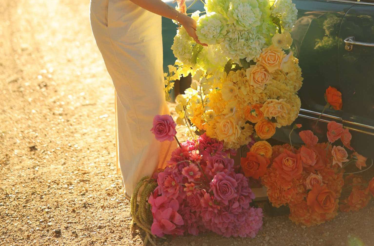 Woman arranging flowers next to a vintage car on a sunny day